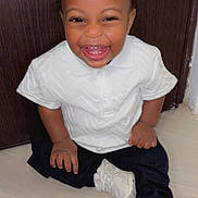 Jayson a rejoint le concours — aidez-le/la à gagner de superbes lots ! baby, black_pants, casual_clothing, child, cute, expression, floor, fun, happy, indoor, joyful, person, portrait, sitting, smile, sneakers, toddler, white_shirt, wooden_door, young_child