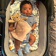 Jace joined the competition — help win amazing prizes! baby, stroller, plush_toy, blanket, giraffe_pattern, cushion, blue_socks, curly_hair, infant, cute, child, indoor, soft_toy, person, face, sleeping_area, cozy, comfort, resting, portrait