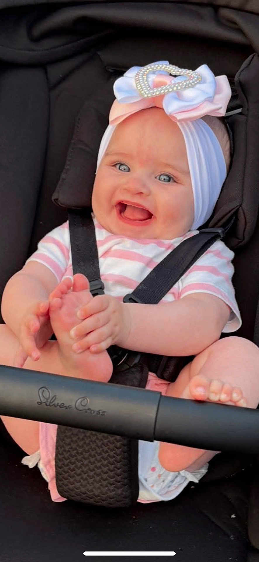 Ariya joined the competition — help win amazing prizes! baby, smiling, blue_eyes, headband, heart_decoration, stroller, car_seat, happy, child, infant, cute, clothing, stripes, foot, hand, person, seatbelt, black_background, pink, white