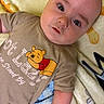 baby, infant, face, eyes, shirt, clothing, blanket, winnie_the_pooh, cartoon, lying_down, cute, child, skin, expression, indoors, toddler, young_child, person, soft_texture, comfort