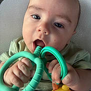 Cameron is registered to the contest to win money with this photo: baby, child, teething_toy, green, yellow, hand, face, mouth, curious, infant, closeup, cute, grip, expression, indoor, clothing, person, toy, skin, head