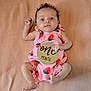 baby, infant, one_month, pink_clothing, strawberry_pattern, wooden_sign, lying_down, blanket, cute, small_hands, small_feet, face, eyes, expression, newborn, child, portrait, indoors, soft_texture, baby_girl