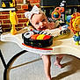 Maisie is registered to the contest to win money with this photo: baby, child, bow, activity_center, toy, smile, indoor, carpet, brick_wall, colorful, play, infant, happy, person, face, foot, headband, plastic_toy, home, cute