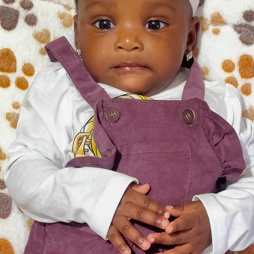 Chimamanda is registered to the contest to win money with this photo: accessories, baby, bodypart, bonnet, cap, clothing, dress, face, finger, hand, happy, hat, head, longsleeve, person, photography, portrait, sitting, sleeve, smile