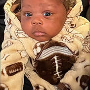 Damian joined the competition — help win amazing prizes! baby, child, face, curly_hair, hoodie, fleece, sports_pattern, football, soccer_ball, brown_skin, large_eyes, cozy, warm_clothing, infant, person, portrait, indoor, couch, blanket, cute