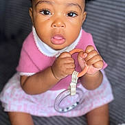 Nellya a rejoint le concours — aidez-le/la à gagner de superbes lots ! baby, child, curly_hair, pink_clothing, toy, ring, white_sandals, open_mouth, wide_eyes, sitting, indoor, close_up, cute, infant, hands, face, footwear, person, portrait, texture