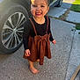 toddler, child, smiling, barefoot, dress, bow, car, wheel, concrete, outdoor, sunlight, happy, person, clothing, sidewalk, grass, daylight, cute, young, standing