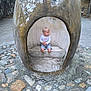 Léo participe au concours pour gagner de l'argent avec cette photo : toddler, child, barefoot, stone_structure, crown_shape, outdoor, backyard, cobblestone, fence, tree, leaves, shirt, shorts, sitting, weathered, concrete, playground, young_child, daylight, casual_clothing