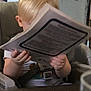child, blonde_hair, high_chair, booklet, reading, hands, panda_face, indoor, table, seatbelt, curious, young_child, paper, furniture, decor, toddler, person, close_up, seat, casual