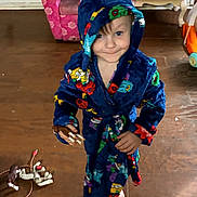 Josiah is registered to the contest to win money with this photo: child, kid, robe, hooded, barefoot, indoor, wooden_floor, toy, smile, face, person, furniture, living_room, playful, colorful_clothing, floor, foot, expression, cute, standing