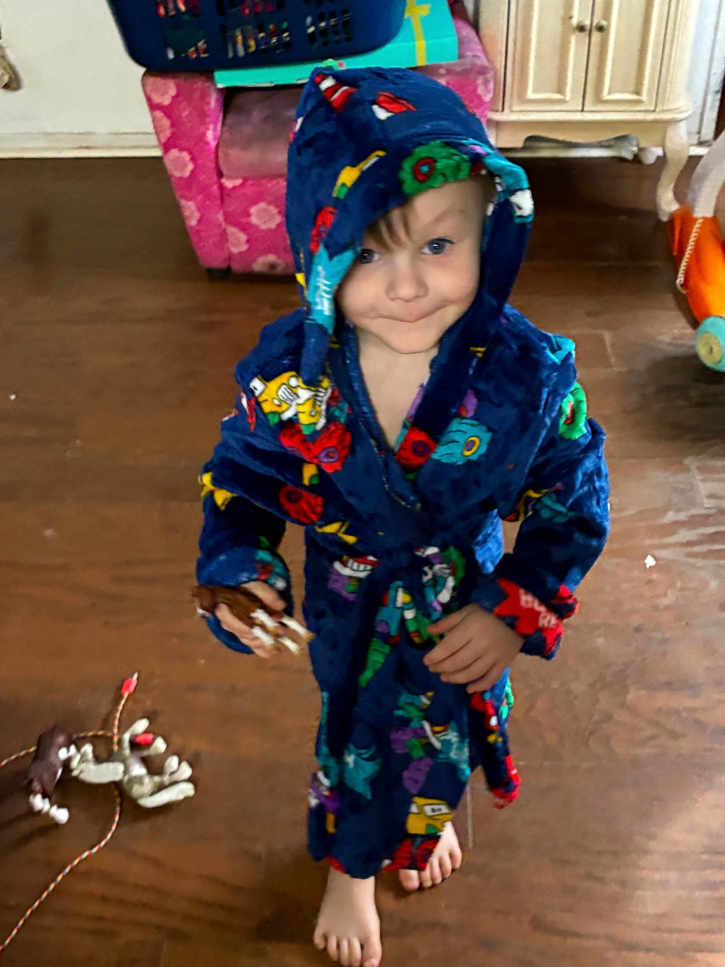 Josiah is registered to the contest to win money with this photo: child, kid, robe, hooded, barefoot, indoor, wooden_floor, toy, smile, face, person, furniture, living_room, playful, colorful_clothing, floor, foot, expression, cute, standing