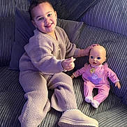 Alaya-Jay joined the competition — help win amazing prizes! child, toddler, doll, couch, knitwear, slippers, indoor, plush, smile, happy, cozy, baby_doll, pink_clothing, furniture, portrait, seated, playful, home, soft_lighting, corduroy