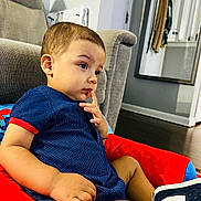 Leo is registered to the contest to win money with this photo: toddler, child, blue_outfit, red_cushion, indoor, living_room, couch, mirror, reflection, floor, sock, shoe, person, furniture, contemplative, seated, casual, home, clothing, young_child