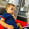 toddler, child, blue_outfit, red_cushion, indoor, living_room, couch, mirror, reflection, floor, sock, shoe, person, furniture, contemplative, seated, casual, home, clothing, young_child