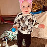 toddler, child, pink_bow, headband, minnie_mouse, sweater, blue_ball, mismatched_socks, carpet, blanket, toy, indoor, person, clothing, footwear, smile, face, play, camouflage_jacket, home