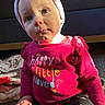 Scarlett is registered to the contest to win money with this photo: toddler, child, baby, headband, pink, shirt, text, sitting, floor, indoor, sunlight, face, clothing, pattern, heart, curious, portrait, person, cute, casual