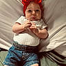 baby, infant, child, red_bow, headband, white_shirt, denim_shorts, bed, pillow, blanket, hands, face, looking_at_camera, indoors, cute, lying_down, skin, expression, wide_eyes, clothing