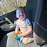 toddler, child, car_seat, snack, smile, sunlight, window, trees, clothing, shorts, shirt, happy, seat, interior, vehicle, daylight, portrait, young_child, sitting, cute