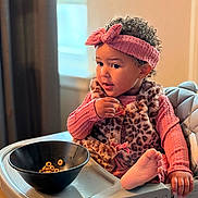 Dakota joined the competition — help win amazing prizes! toddler, child, high_chair, cereal, bowl, pink_headband, leopard_print, vest, curly_hair, indoor, window, table, foot, hand, clothing, person, snack, young_child, seat, expression