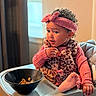 bowl, cereal, child, clothing, curly_hair, expression, foot, hand, high_chair, indoor, leopard_print, person, pink_headband, seat, snack, table, toddler, vest, window, young_child