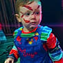 Freddie is registered to the contest to win money with this photo: child, face_paint, colorful_clothing, overalls, striped_shirt, young_child, indoor, blurred, low_light, portrait, face, hand, expression, costume, playful, scratches, red_paint, green, blue, yellow