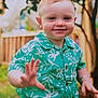 toddler, child, smiling, hand, green_shirt, floral_pattern, outdoor, garden, fence, happy, portrait, person, cute, young_child, short_hair, summer, nature, tree, casual_clothing, daylight