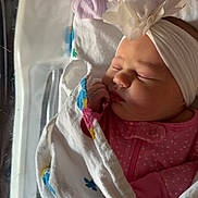 Willow is registered to the contest to win money with this photo: newborn, baby, sleeping, blanket, hospital, bassinet, headband, flower, pink_clothing, infant, wrapped, sleep, cute, peaceful, indoor, child, portrait, resting, tiny_hand, soft_light