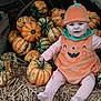 baby, child, pumpkin_costume, pumpkins, straw, autumn, orange, hat, smile, face, striped_clothing, festive, seasonal, cute, sitting, outdoor, harvest, holiday, person, fun