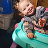 baby_walker, bucket, child, colorful, curly_hair, cute, flooring, happy, household_items, indoor, person, pigtails, plastic, playful, portrait, sitting, smiling, sweatshirt, toddler, young_child