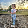 Wrenlee joined the competition — help win amazing prizes! toddler, child, overalls, boots, curly_hair, outdoor, sunset, park, wood_chips, grass, trees, sky, clouds, house, fence, nature, person, young_child, casual_clothing, daylight