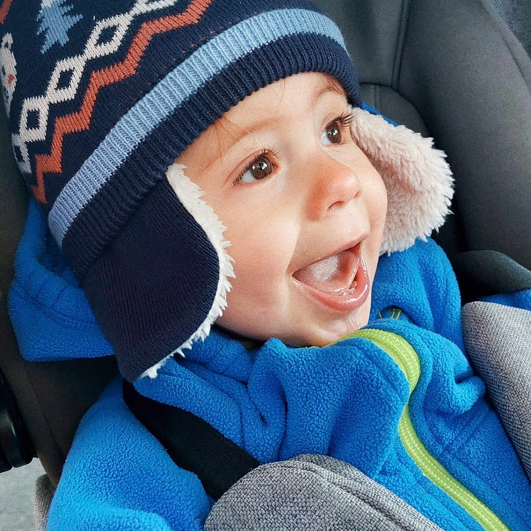 Maël a rejoint le concours — aidez-le/la à gagner de superbes lots ! baby, blue_jacket, car_seat, child, clothing, cozy, cute, expression, face, happy, headwear, indoors, joyful, person, seatbelt, smiling, toddler, transportation, warm, winter_hat