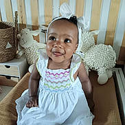 Isalya participe au concours pour gagner de l'argent avec cette photo : baby, child, smiling, white_dress, headband, plush_toy, sheep_toy, brown_cushion, indoor, furniture, happy, cute, portrait, infant, seated, person, baby_clothes, decor, playroom, soft_toy
