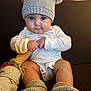 Keomi joined the competition — help win amazing prizes! baby, infant, hat, knit_hat, pom_poms, booties, couch, hand, adult_hand, bracelets, cute, chubby_cheeks, sitting, indoor, cozy, clothing, person, portrait, warm, comfort