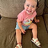 toddler, child, smiling, sitting, couch, pink_shirt, blue_shorts, white_sandals, happy, indoors, cute, portrait, young_child, face, person, hair_bows, small_earrings, footwear, red_bracelet, casual_clothing