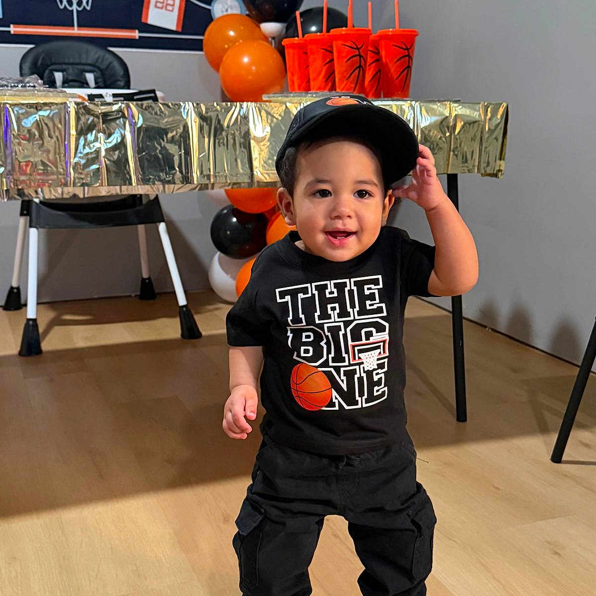 Luisniel joined the competition — help win amazing prizes! background, balloons, basketball_theme, black_clothing, boy, cap, celebration, child, cups, decorations, floor, happy, indoor, party, smiling, sneakers, sportswear, standing, table, toddler