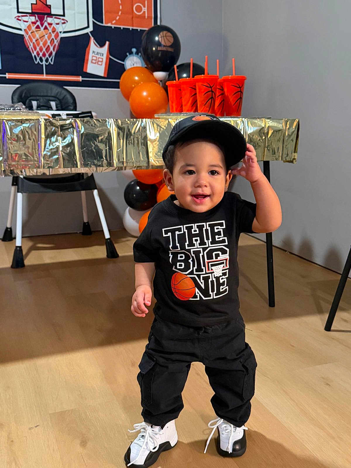 Luisniel joined the competition — help win amazing prizes! background, balloons, basketball_theme, black_clothing, boy, cap, celebration, child, cups, decorations, floor, happy, indoor, party, smiling, sneakers, sportswear, standing, table, toddler