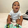baby, child, smiling, sitting, white_onesie, colorful_shoes, bed, indoor, happy, cute, young_child, playful, toddler, infant, human, person, casual_clothing, fun, expression, hair