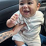 baby, child, smiling, happy, infant, striped_clothing, sneakers, car_interior, tattoo, hand, person, cute, face, seat, window, daylight, jeans, white_socks, closeup, portrait