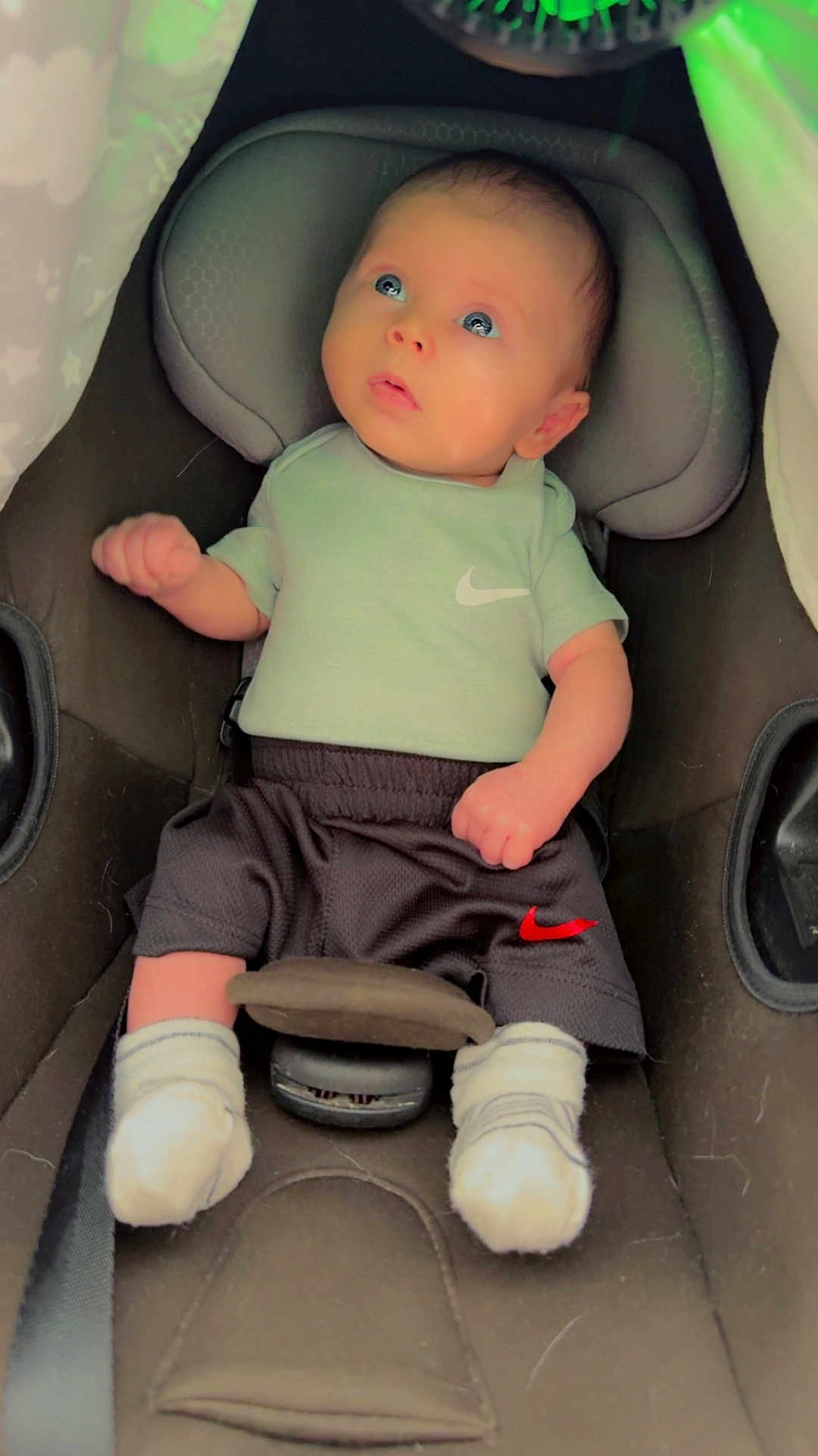 Kayden is registered to the contest to win money with this photo: baby, infant, car_seat, nike, clothing, socks, child, portrait, indoors, seatbelt, cute, young, person, apparel, seat, head_support, looking_up, small, soft_light, casual
