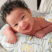 Zayden joined the competition — help win amazing prizes! baby, smiling, curly_hair, pillow, animal_pattern, bedroom, blanket, infant, happy, cute, child, resting, indoors, soft_texture, face, person, young, comfort, toddler, expression
