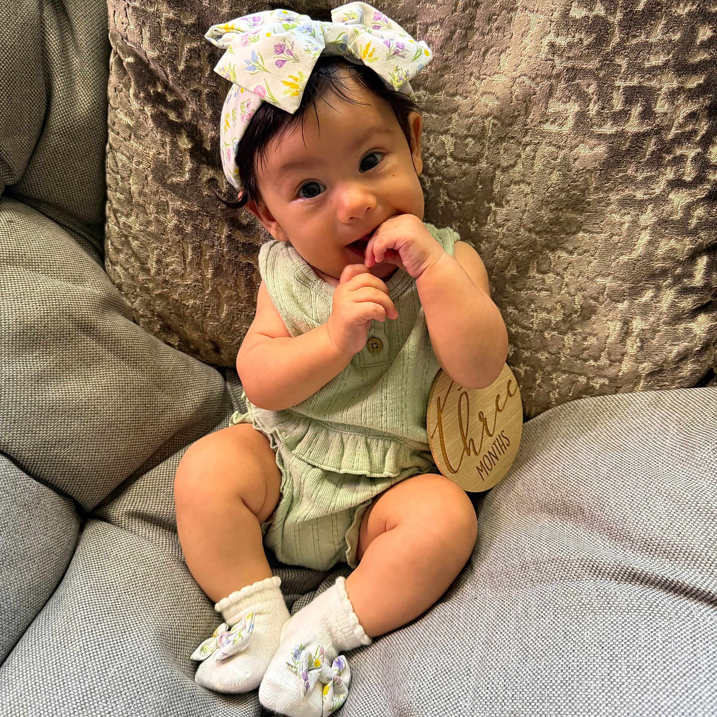 Sosa is registered to the contest to win money with this photo: baby, bow, child, clothing, comfortable, couch, curious, cute, fingers, happy, headband, indoor, infant, portrait, sitting, smiling, socks, soft_lighting, three_months, wooden_sign