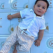 Elio a rejoint le concours — aidez-le/la à gagner de superbes lots ! baby, barefoot, casual_clothing, child, curly_hair, cute, happy, indoors, infant, laying_down, patterned_background, people, play_mat, portrait, relaxed, smiling, striped_pants, toddler, white_shirt, young_child