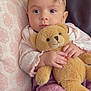baby, teddy_bear, pink_bow, pillow, couch, infant, soft_toy, clothing, headband, cute, child, portrait, indoor, cozy, hands, face, expression, knitwear, seated, young_child