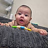 baby, infant, child, portrait, face, eyes, open_mouth, smiling, indoor, blanket, couch, furniture, toy, teething_toy, clothing, hands, sitting, home, closeup, photography