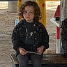 Lina a rejoint le concours — aidez-le/la à gagner de superbes lots ! bench, boots, casual_clothing, child, colorful_poles, curly_hair, daytime, expressionless, ground, holding_object, jacket, natural_light, outdoor, person, playground, rustic, shelter, sitting, wooden_bench, young_child