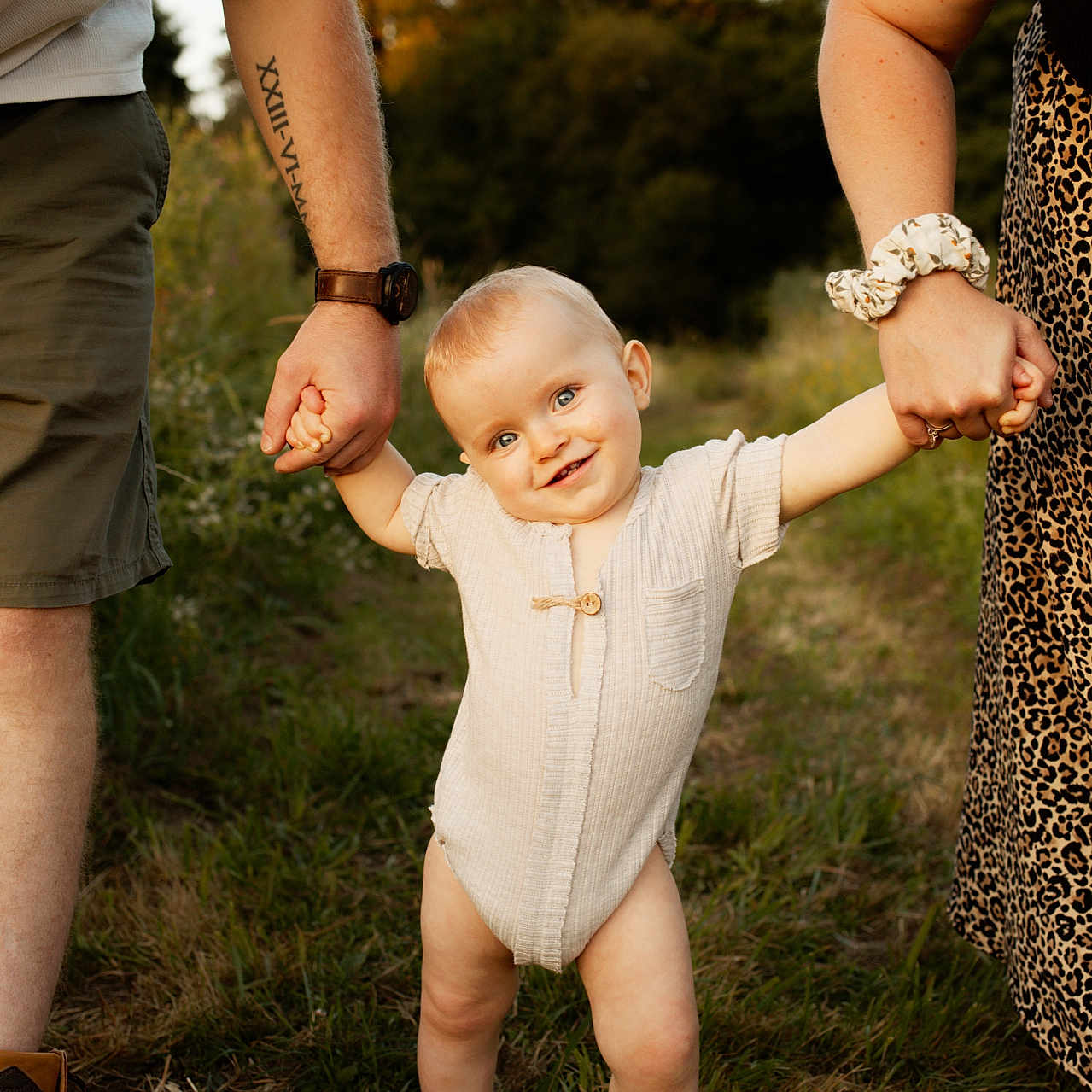 Léo a rejoint le concours — aidez-le/la à gagner de superbes lots ! adult_arms, casual_clothing, child, family, footwear, grass, happy, holding_hands, leopard_print, nature, onesie, outdoor, playful, portrait, scrunchie, smiling, sunlight, tattoo, toddler, watch