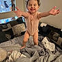 toddler, child, smiling, arms_outstretched, bed, blanket, pillow, curly_hair, indoor, happy, clothing, fabric, cozy, home, person, playful, cute, expression, young, room