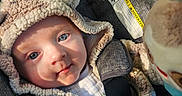 Bryce is registered to the contest to win money with this photo: baby, infant, child, stroller, car_seat, harness, portrait, smiling, blue_eyes, winter_clothing, hat, blanket, plush, cozy, seated, outdoor, close_up, safety_label, fabric, vehicle