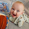 baby, child, infant, smiling, laughing, portrait, face, blue_eyes, light_hair, sitting, play_area, toy, colorful, orange_cushion, blanket, indoors, candid, happy, clothing, baby_bib