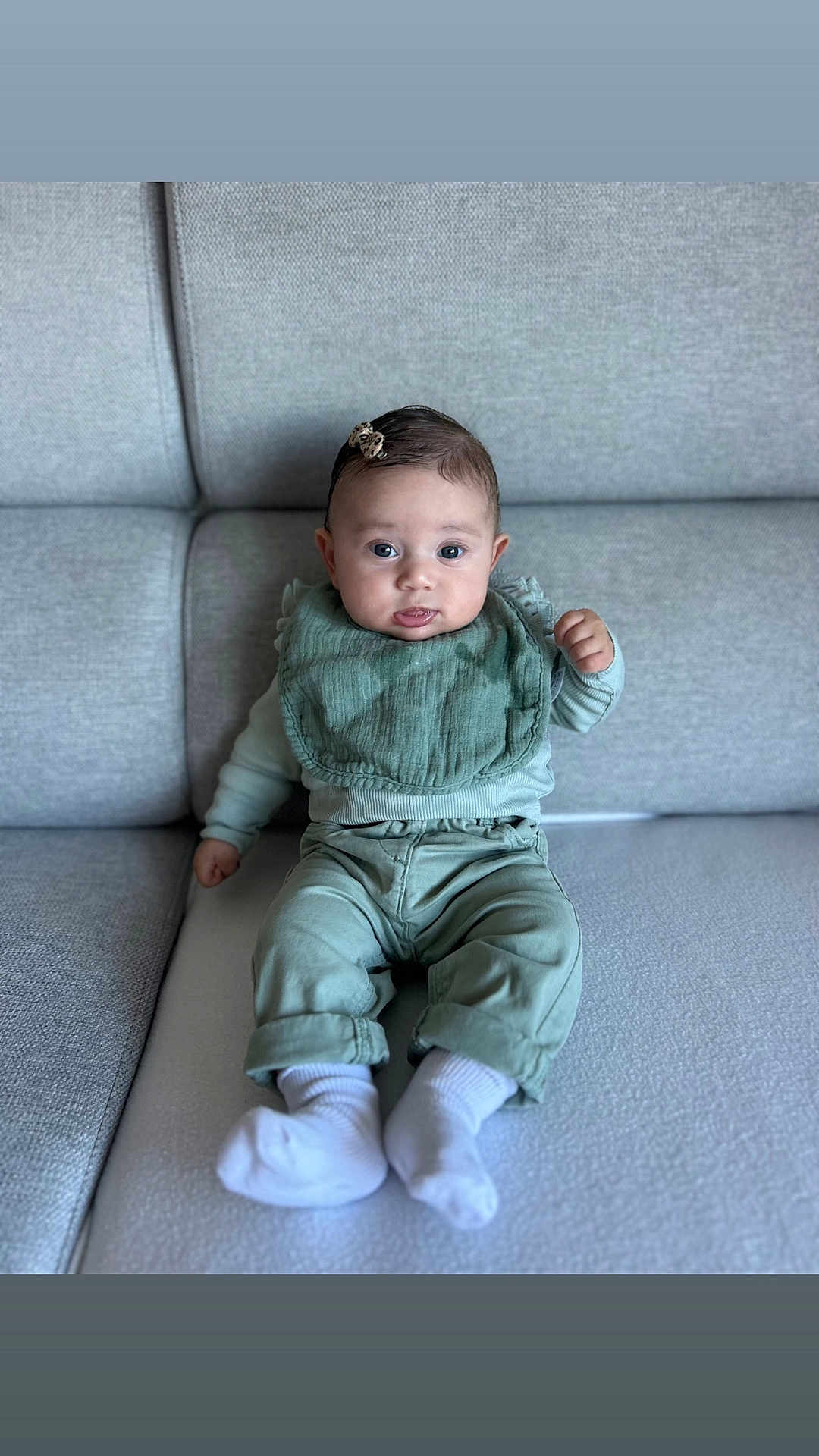 Giulia participe au concours pour gagner de l'argent avec cette photo : baby, infant, child, sitting, couch, sofa, clothing, bib, hair_clip, white_socks, green_outfit, indoor, portrait, cute, young, person, furniture, face, head, expression